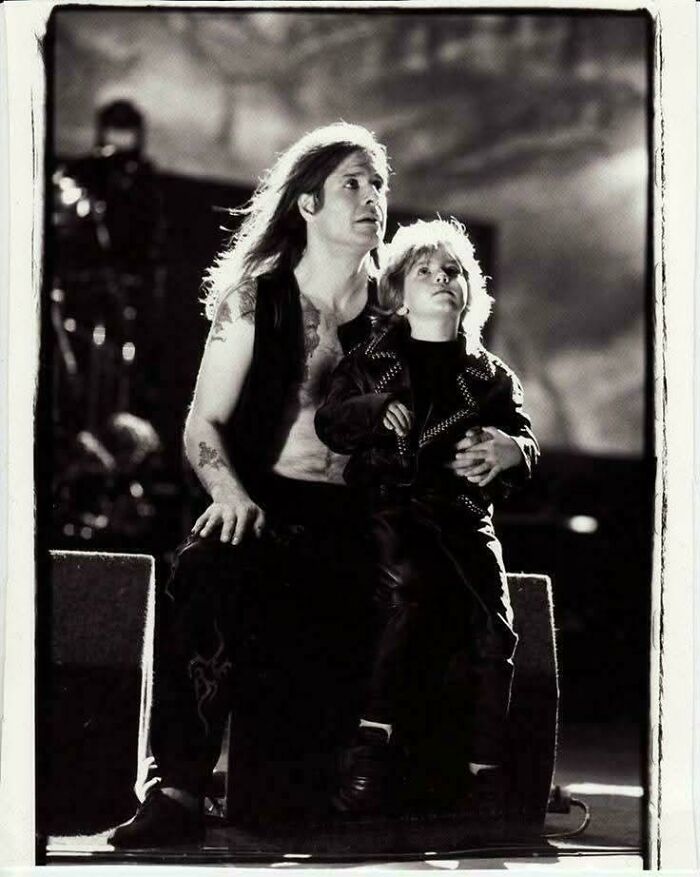 Black and white accidental Renaissance photo of a man with long hair and child in studded leather jacket sitting together.