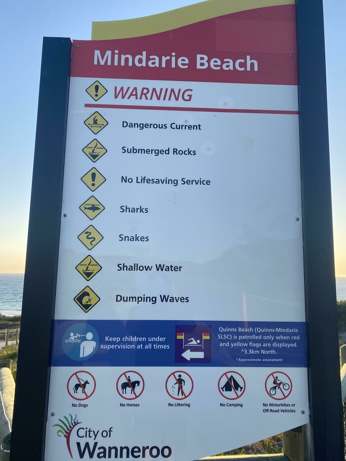 Warning sign at Mindarie Beach listing dangers like sharks, snakes, and dangerous currents found at the beach.