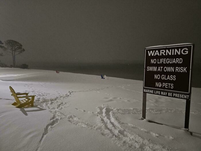 Snow-covered beach at night with warning sign and empty chairs, an interesting and bizarre beach discovery scene.