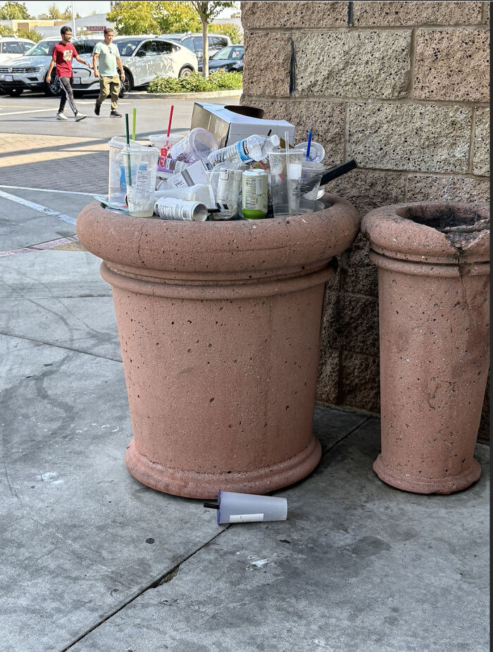 Overflowing trash bin with discarded consumer cups and packaging, illustrating the impact of excessive consumerism in public spaces.