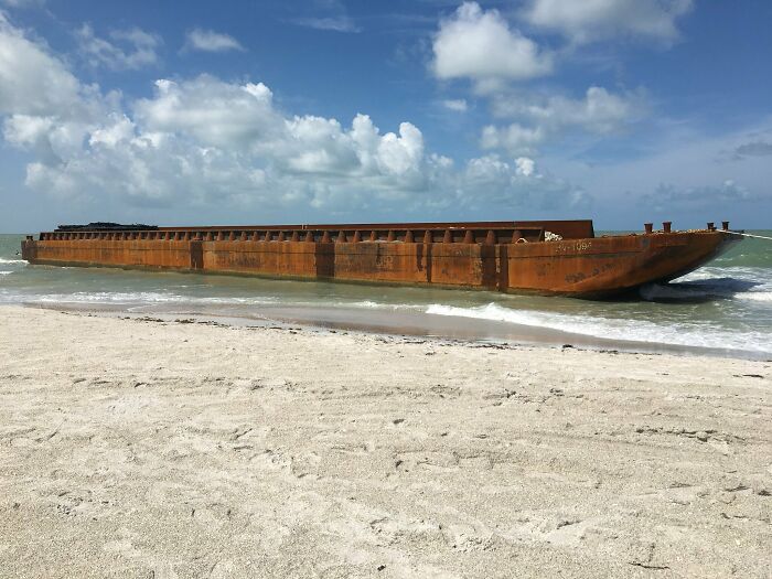 Rusty large metal barge washed ashore on sandy beach with waves and blue sky, an interesting and bizarre thing found at the beach.