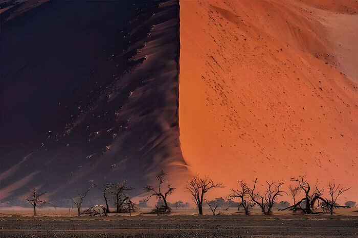 A dramatic view of an extremely large sand dune with a sharp contrast between shaded dark and sunlit orange, eerie.