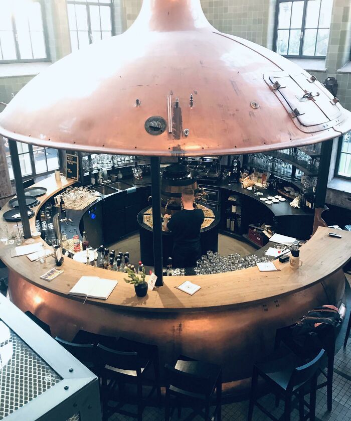 Circular bar with copper hood and wooden counter, bartender preparing drinks in a creative bar setting.