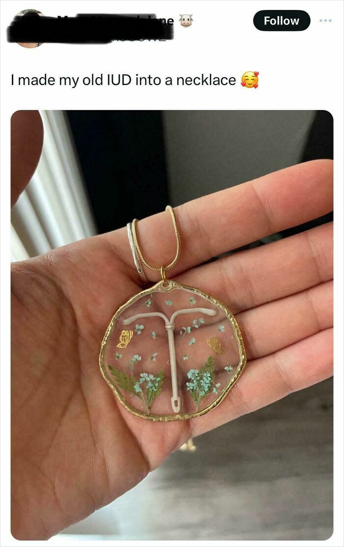 Hand holding a DIY necklace made from an old IUD encased in resin with small flowers, showcasing a DIY disaster.