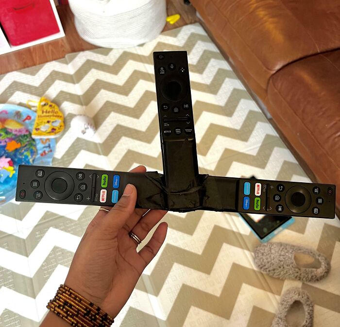 Hand holding a DIY disaster of three taped remote controls joined together, illustrating a museum of mistakes.