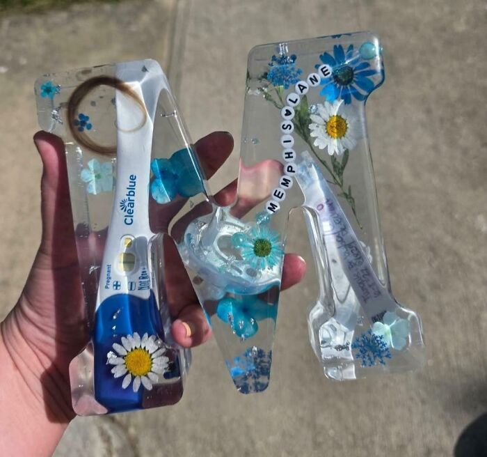 Hand holding resin letters with embedded flowers and a pregnancy test, showing a unique DIY disaster project.