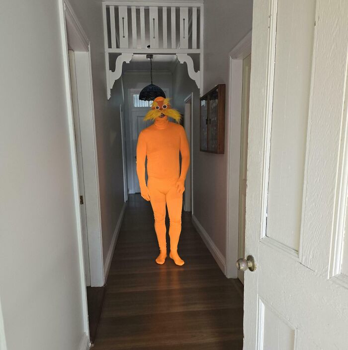 Person in a tight orange DIY costume with added yellow fake mustache and glasses standing in a narrow hallway, a DIY disaster.