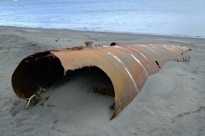 Rusty metal debris partially buried in sand on a beach, an example of bizarre things people found at the beach