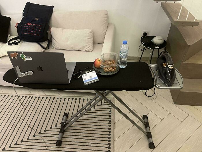 Ironing board repurposed as a laptop desk with snacks, water, and accessories showcasing genius life hacks in use.
