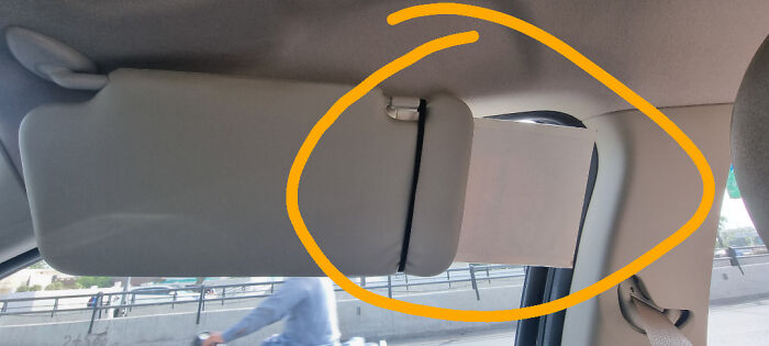 Car sun visor with a rubber band hack holding an extended shade for better sun protection inside the vehicle.
