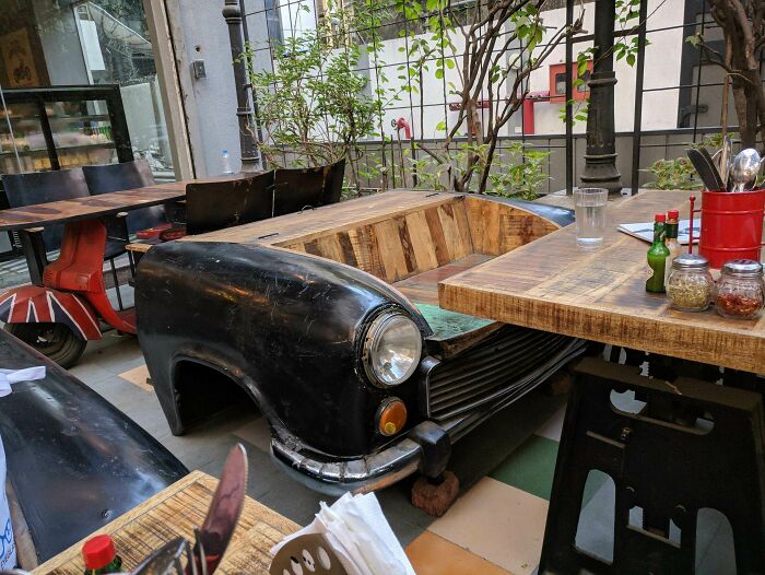 Creative bar seating made from a vintage car front in an outdoor restaurant setting with rustic wooden tables and greenery.