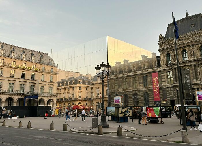 Modern reflective building blending with historic architecture, showcasing perfect matching surroundings in an urban public square.