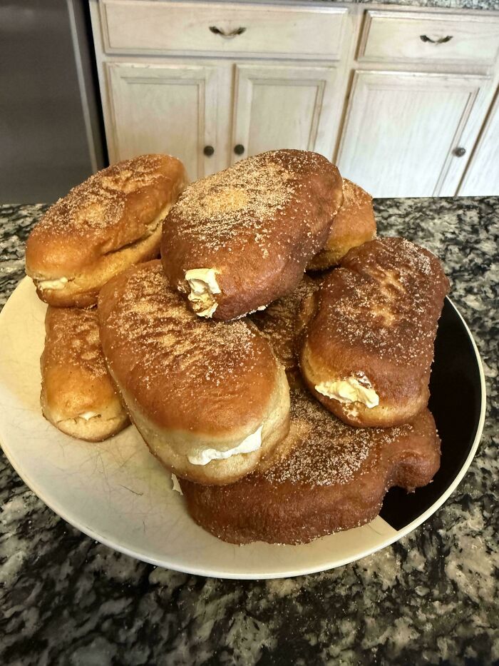 Plate of homemade baked goods filled with cream, sprinkled with sugar, on a kitchen countertop showcasing gorgeous baked treats.
