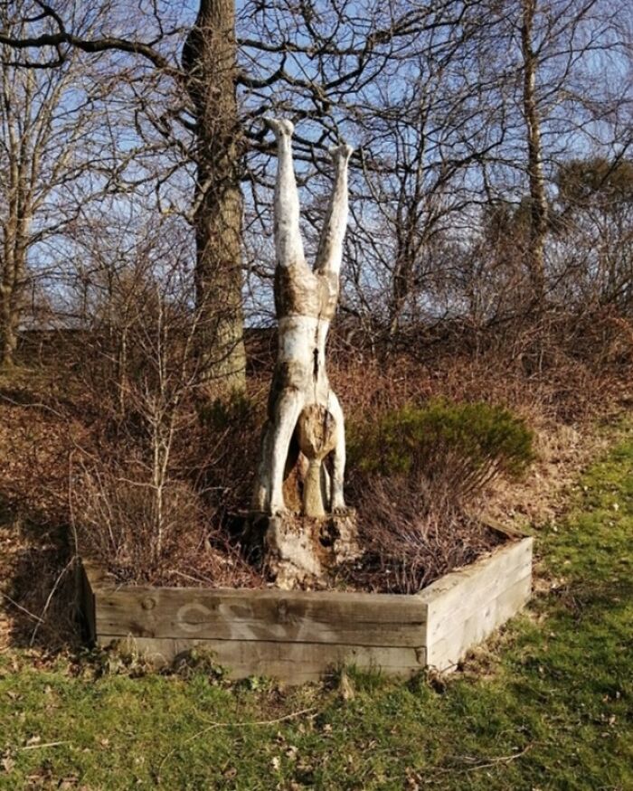Sculpture of a person doing a handstand in a garden, creating a creepy and unsettling moment captured outdoors.