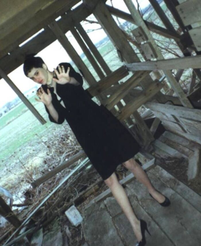 Person in black dress standing in an old wooden structure, captured in a creepy and unsettling moment outdoors.