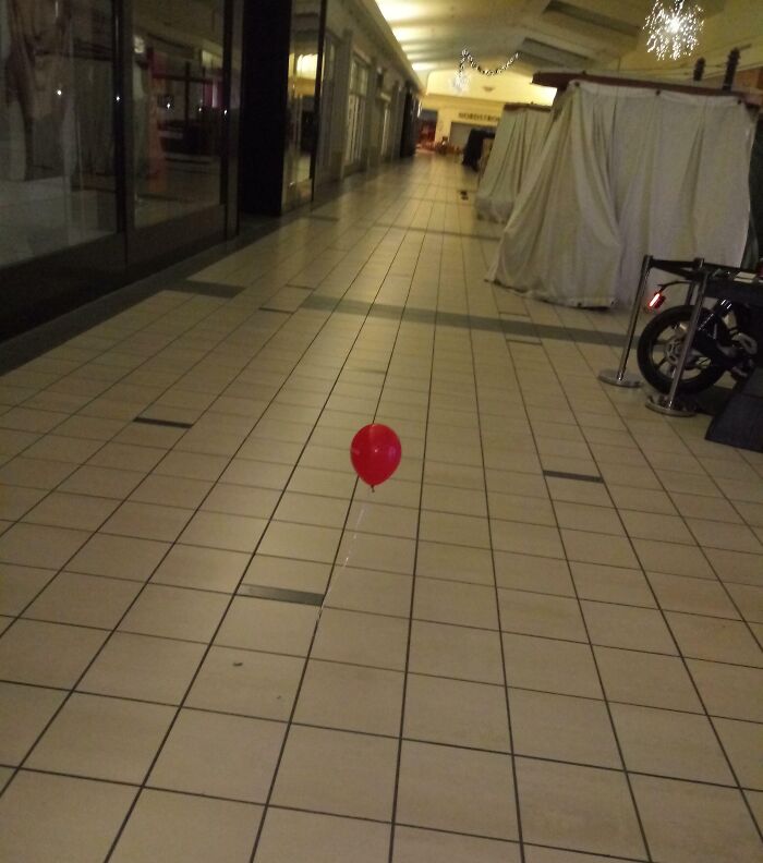 Red balloon floating alone in a deserted hallway, creating a creepy and unsettling moment captured indoors.