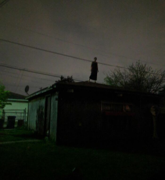 Creepy and unsettling moment with a shadowy figure standing on a roof at night under dark, ominous skies.