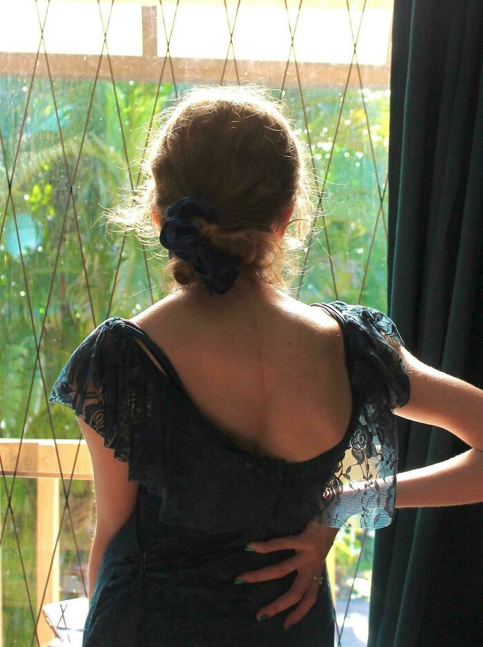 Woman in a lace dress with hair tied back, standing by a window with sunlight highlighting an accidental renaissance photo moment.