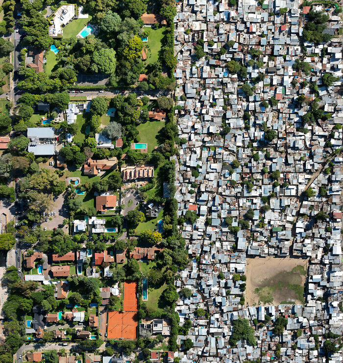 Aerial view contrasting a wealthy green neighborhood with a dense, packed urban slum in a $58 billion ghost city.