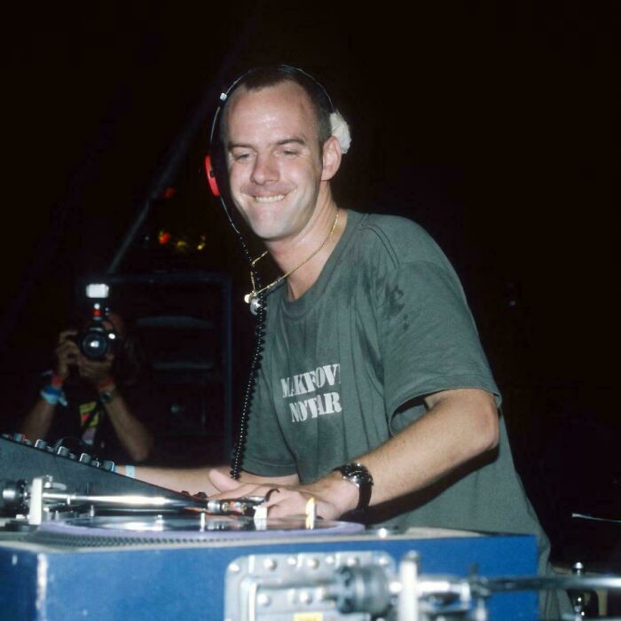 DJ wearing headphones and a green shirt mixing music on turntables, evoking ’90s posts and memories.