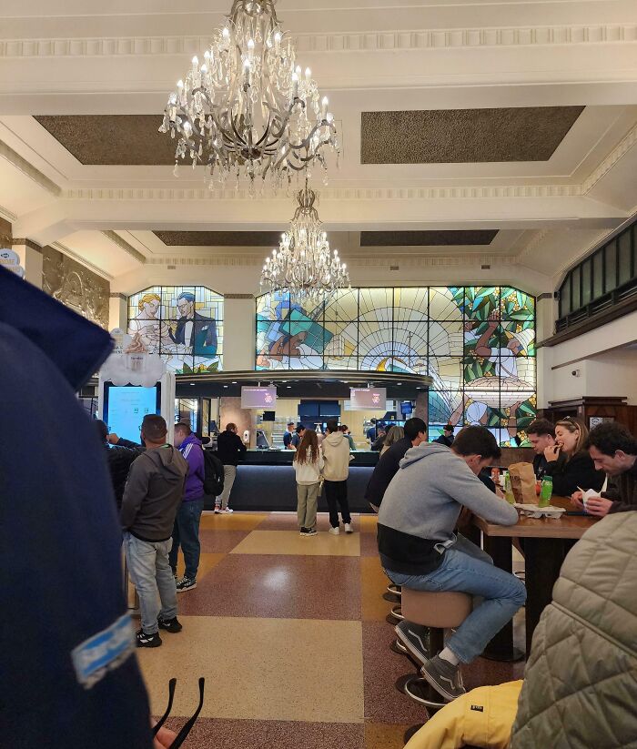 Elegant bar and restaurant interior with chandeliers, stained glass windows, and people dining and ordering food.