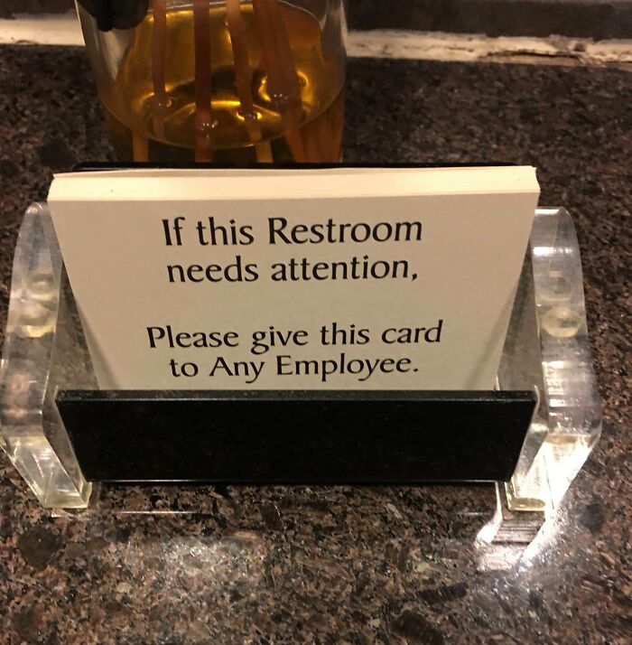 Card on a bar countertop instructing to notify any employee if the restroom needs attention in a creative bar setting.