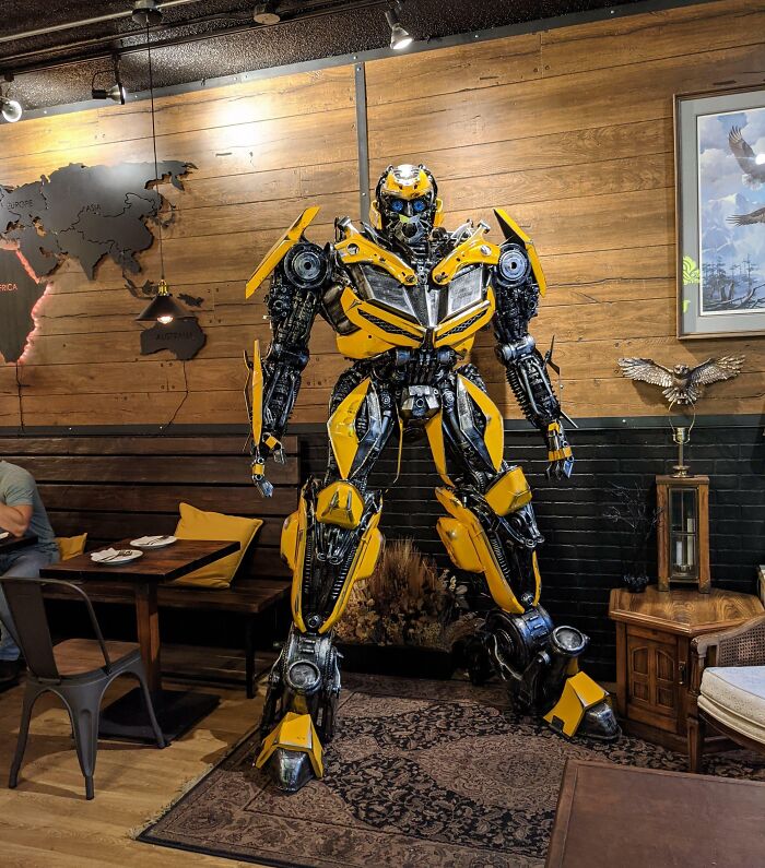 Yellow and black robot sculpture inside a creative bar and restaurant with wooden walls and modern decor.