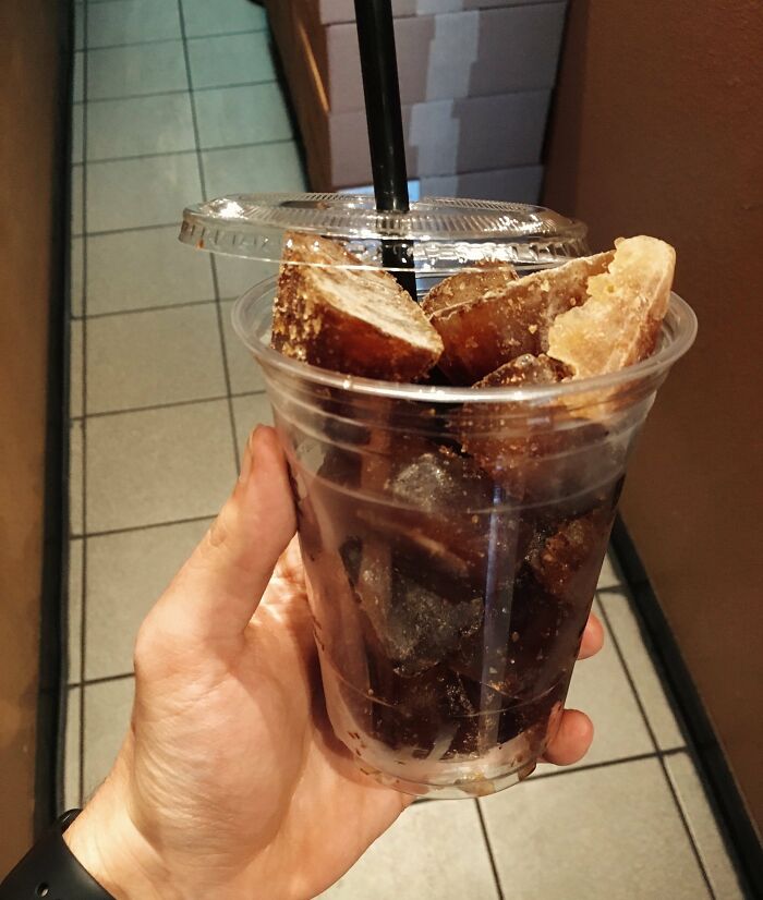 Hand holding a creative iced coffee drink in a clear plastic cup with a straw, featured in bars and restaurants.