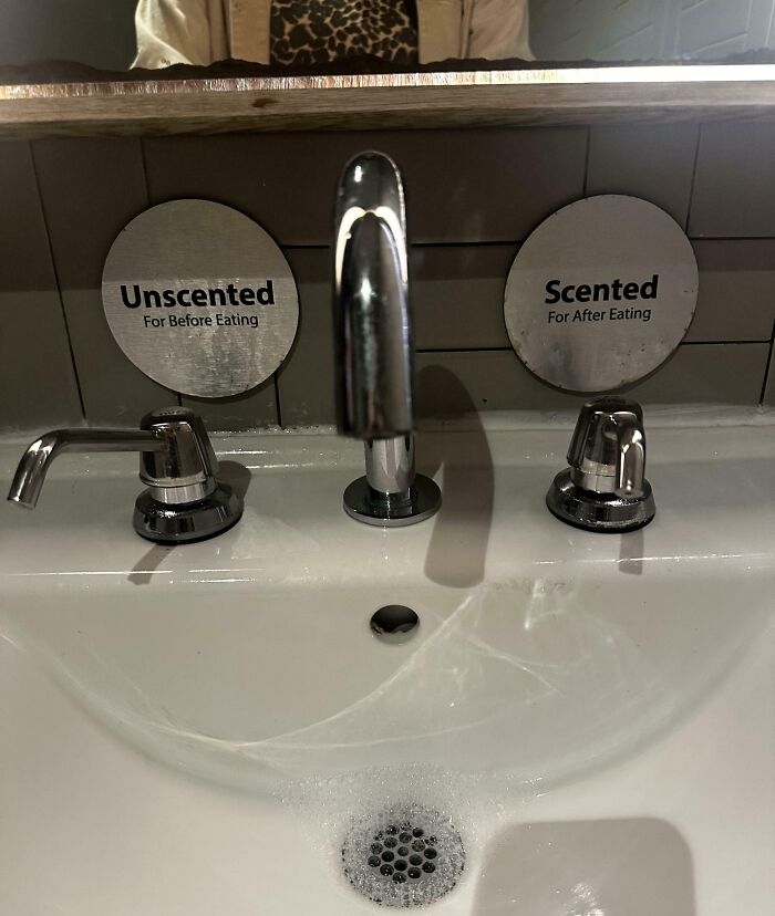 Sink with two soap dispensers labeled Unscented for before eating and Scented for after eating in a creative bar restroom.