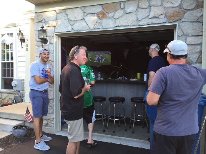 Group of wholesome kind neighbors gathering outside a home patio bar, enjoying drinks and watching a football game together.