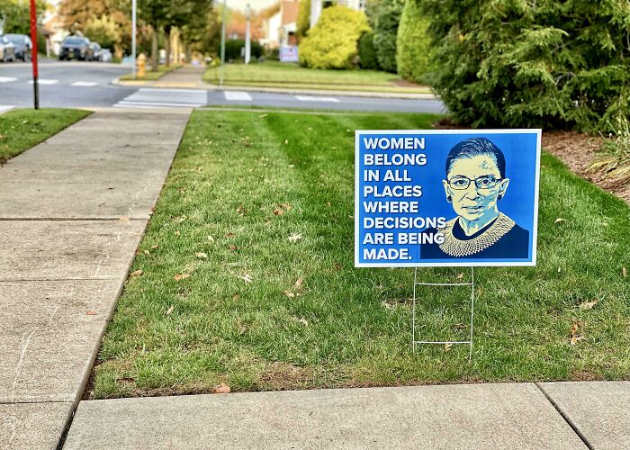 Yard sign with inspirational quote about women’s roles placed on green lawn in a quiet neighborhood by wholesome kind neighbors.