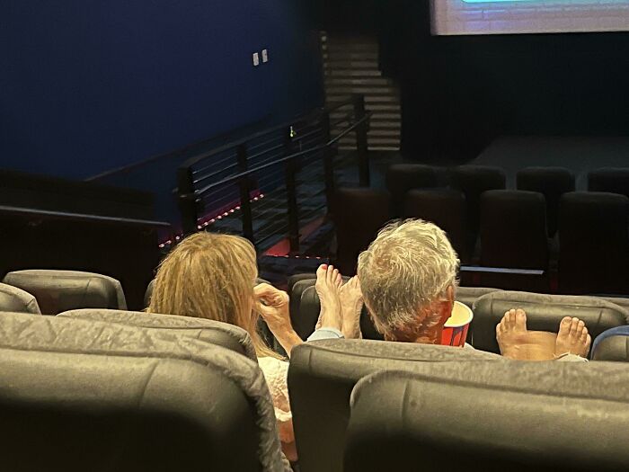 Two people in a movie theater resting their bare feet on seats, showing selfish behavior affecting others nearby.
