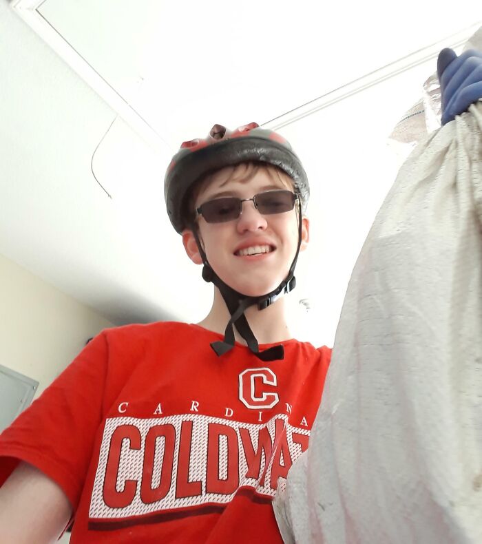 Teen wearing helmet and glasses, smiling while holding a large bag, showing wholesome kind neighbors spirit.