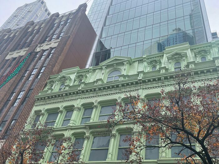 Green historic building contrasted with tall modern glass and brick architecture showcasing old versus modern architecture.