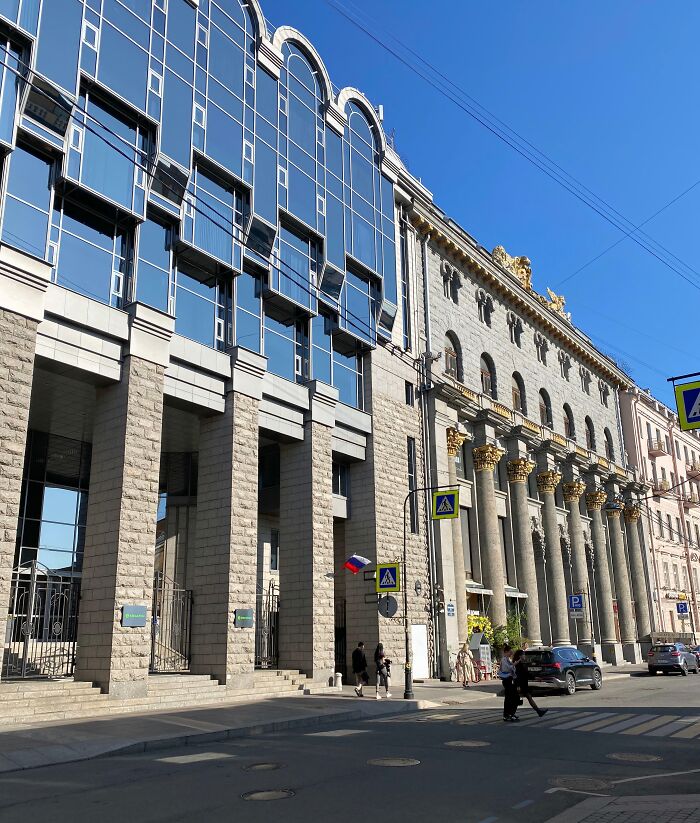Modern glass facade building next to an old classical architecture with stone columns under a clear blue sky.