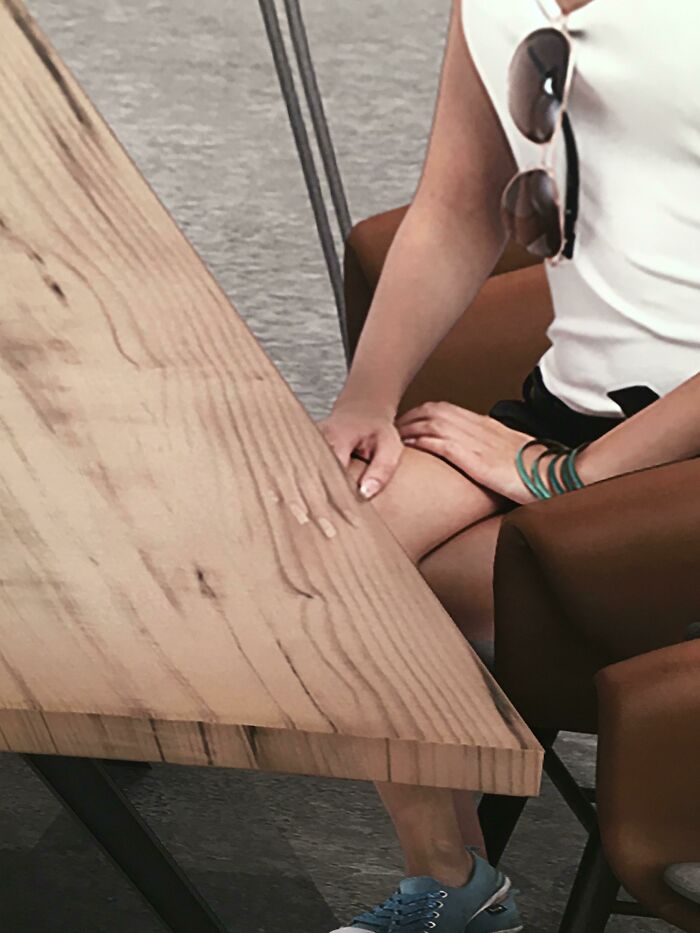 Person sitting at a wooden table Photoshop fail showing distorted missing foot and awkward hand placement in humorous editing error
