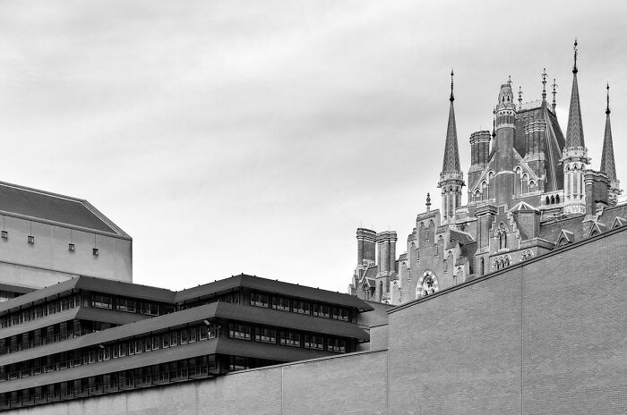 Contrast between old versus modern architecture shown with historic spires behind a blocky, modern building in black and white.
