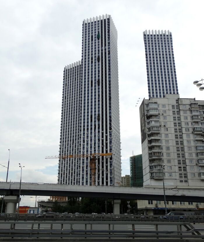 Tall modern skyscrapers with grid-like windows contrast with older, worn apartment buildings in an urban cityscape.