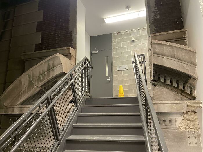 Staircase blending old stone architecture with modern metal railings and concrete walls in an urban building interior.