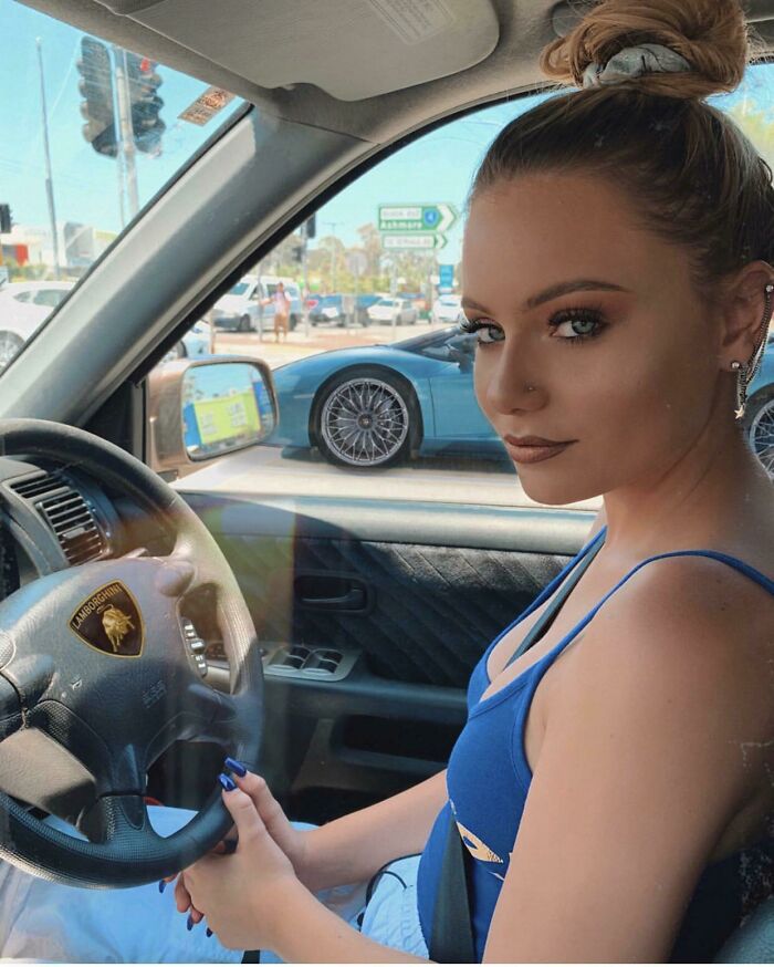 Young woman sitting in a car with a poorly edited steering wheel logo, showcasing glaring Photoshop fails on a sunny day.