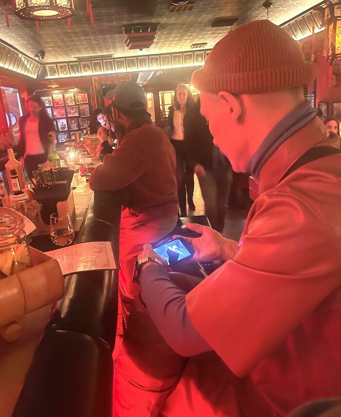 Man in red hat and jacket using phone in crowded bar showing selfish people behavior making life harder for others
