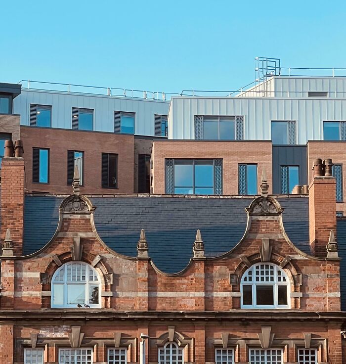 Old versus modern architecture shown with historic brick building in front of sleek contemporary apartment complex under clear sky.