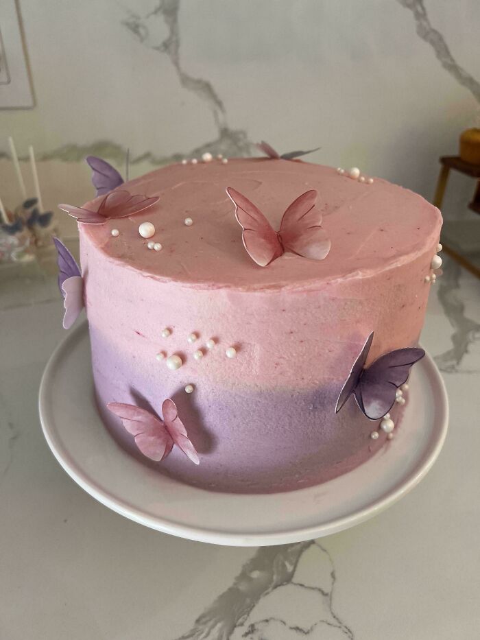 Pink and purple frosted cake decorated with edible butterflies and pearls, showcasing gorgeous baked goods artistry.