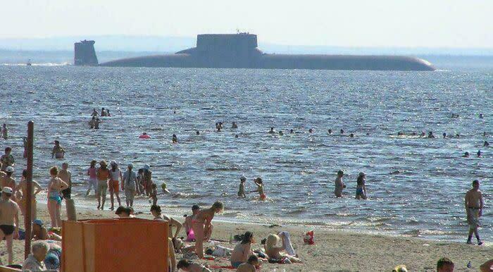 Extremely large things: A huge submarine, an extremely large and scary thing, surfaces near a crowded beach with many swimmers.