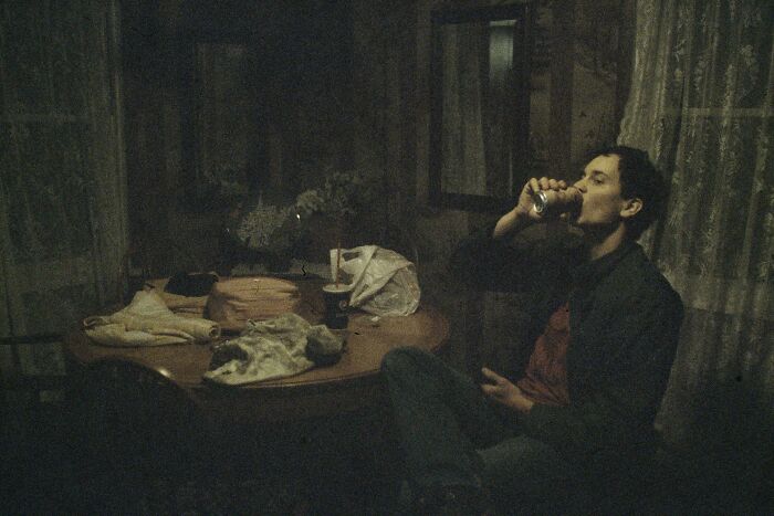 Man sitting at a dimly lit table drinking from a can, capturing the mood of accidental renaissance photos with soft lighting.