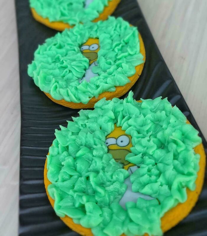 Cookies decorated with green frosting partially revealing ’90s cartoon character images on a black tray, nostalgic ’90s posts theme.