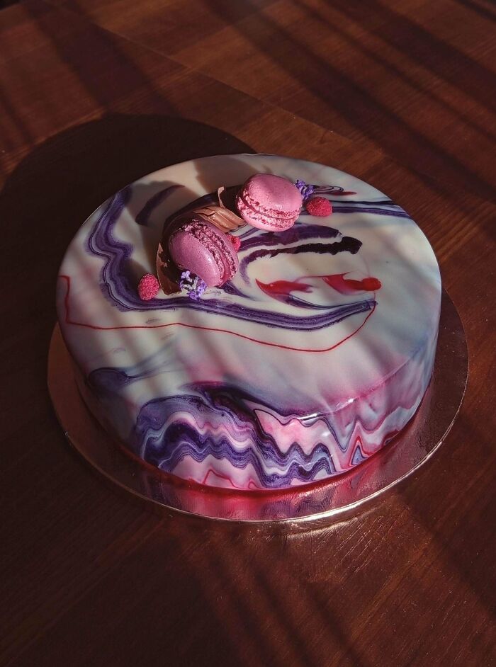 Marble glazed cake with pink macarons and decorative accents showcasing gorgeous baked goods artistry on wooden surface.