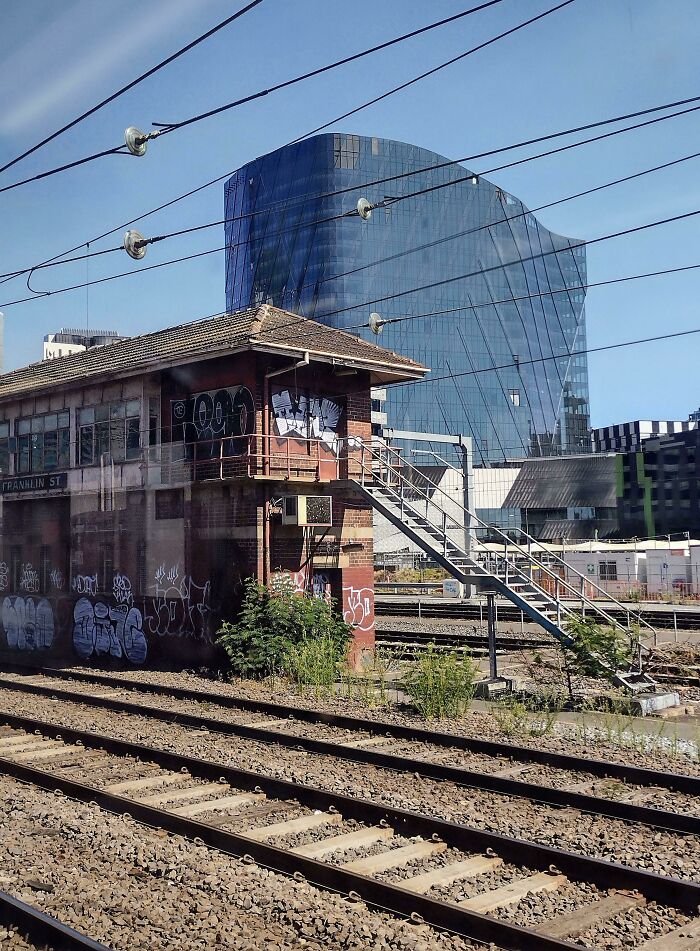 Old versus modern architecture shown by old graffiti-covered building and sleek glass skyscraper near railway tracks.