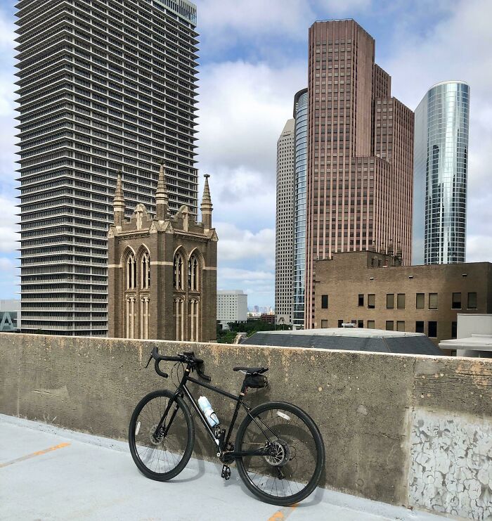 Bicycle parked on rooftop with old gothic-style architecture contrasted against modern skyscrapers in the background.