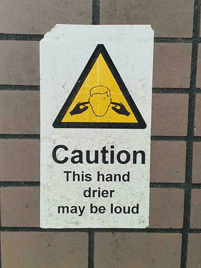 Warning sign on a wall humorously cautioning that the hand dryer may be loud, featuring a playful illustration.